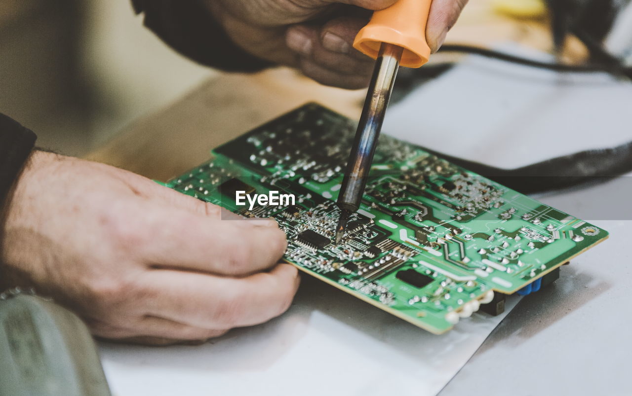 Cropped hands of engineer repairing mother board on table