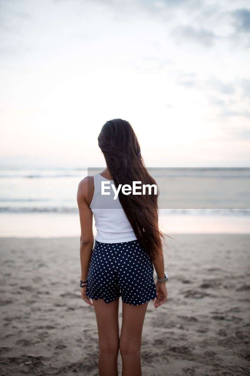 Rear view of mid adult woman standing at beach against sky