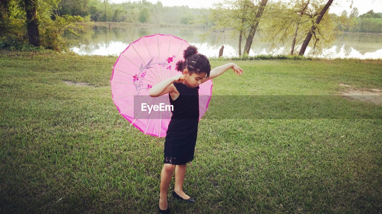 Full length of girl holding umbrella while standing on field