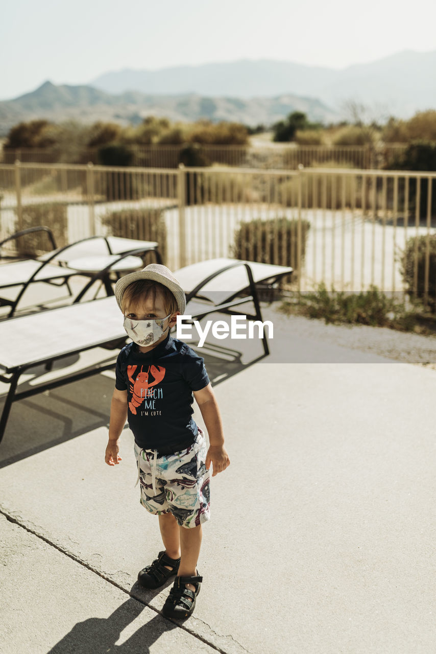 Young toddler boy with mask on standing by pool in palm springs