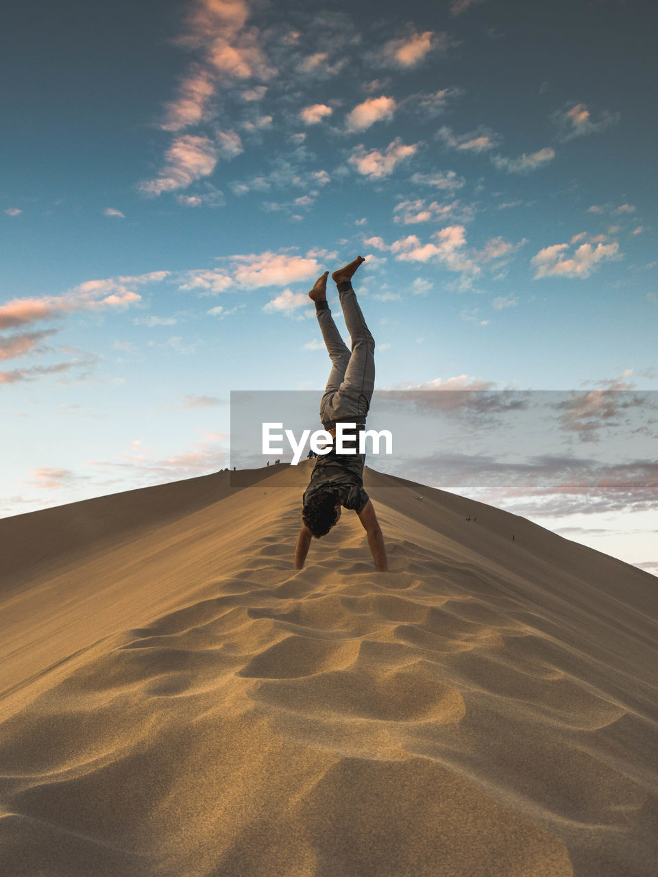 Man doing handstand in sand at dessert against sky