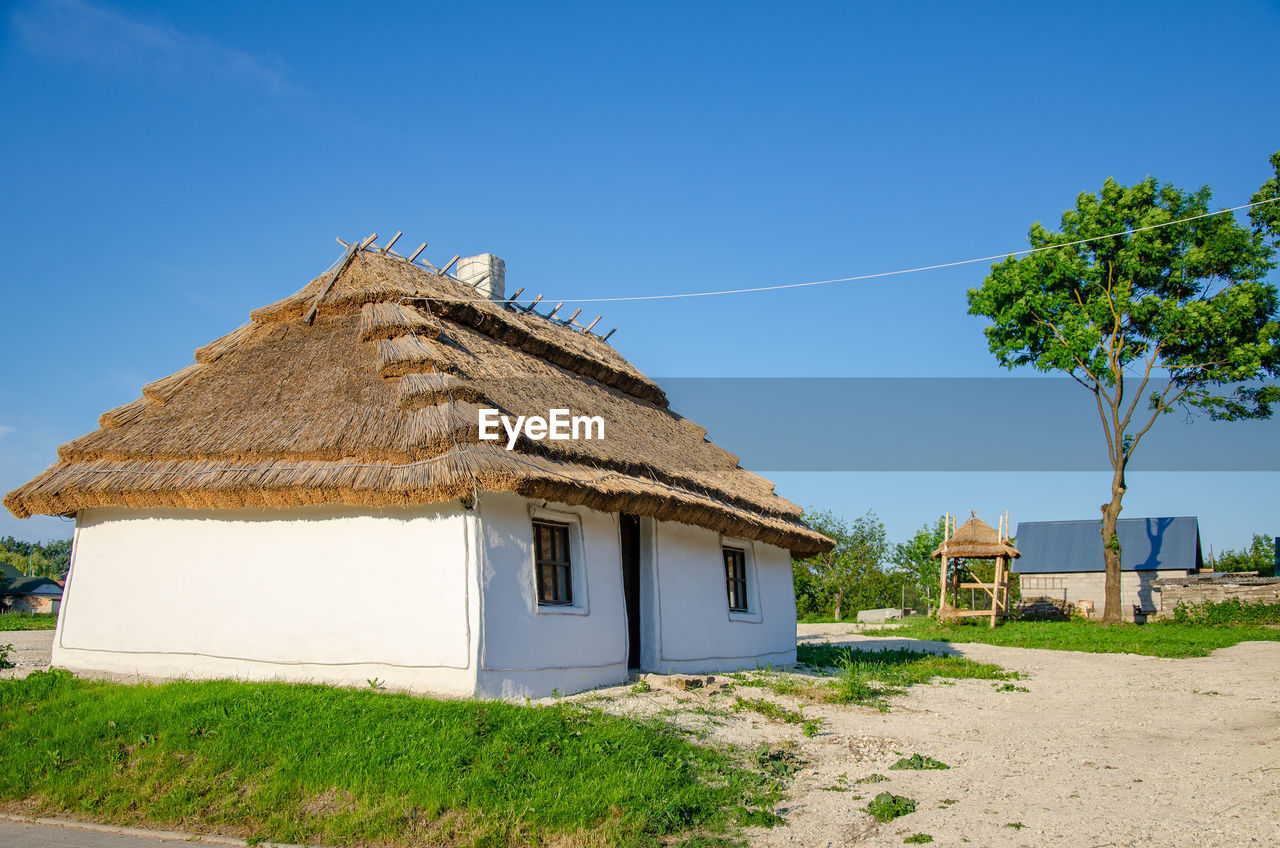 Rural landscape with ancient ukrainian clay house. thatched roof, white walls with lime, chimney.