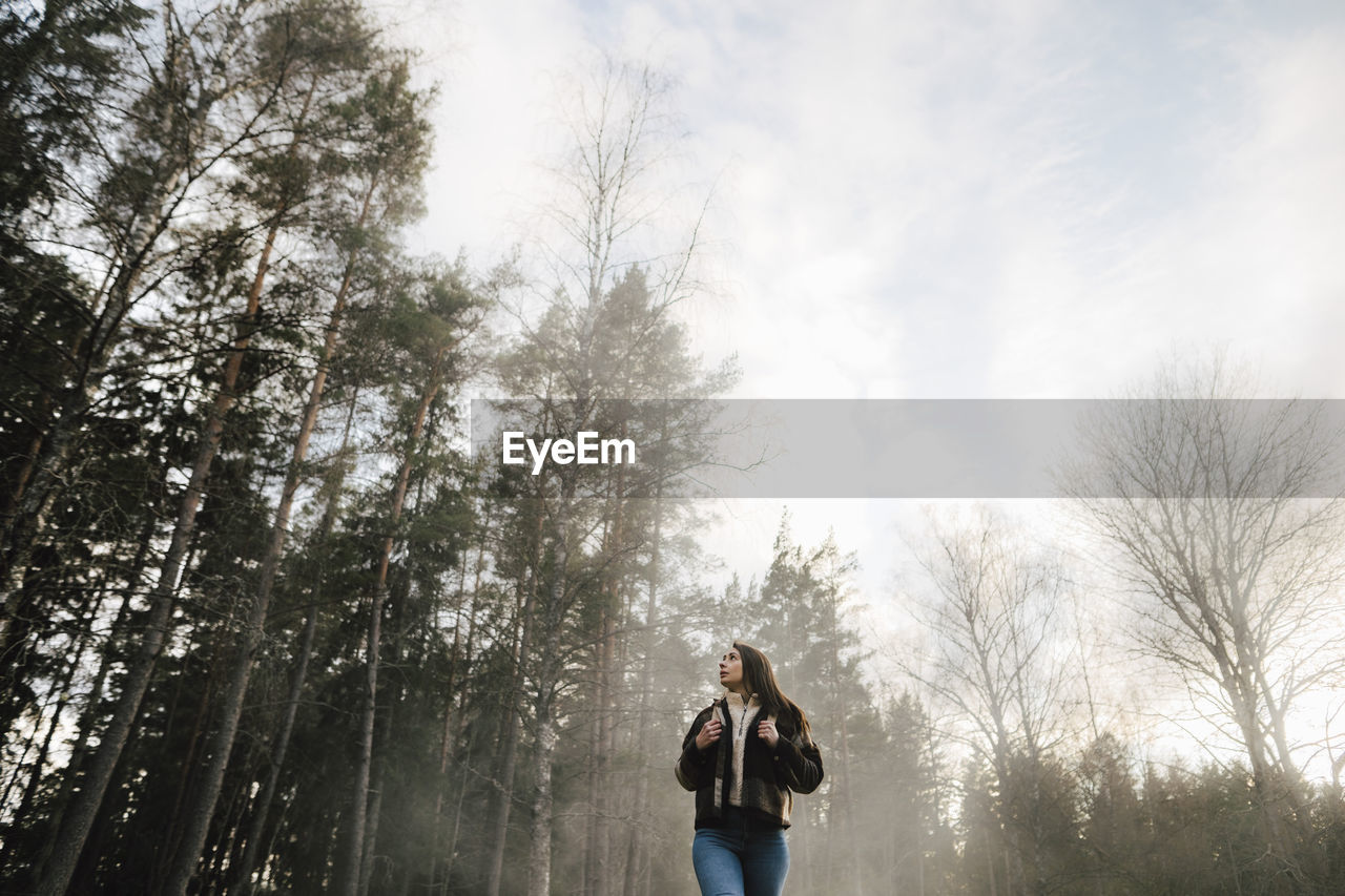 Low angle view of woman walking in forest during foggy weather