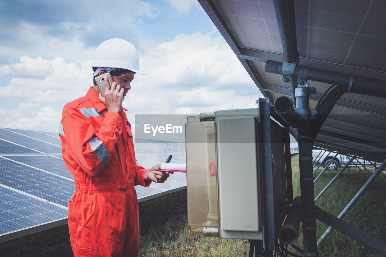 Side view of worker talking on phone while standing by solar panel