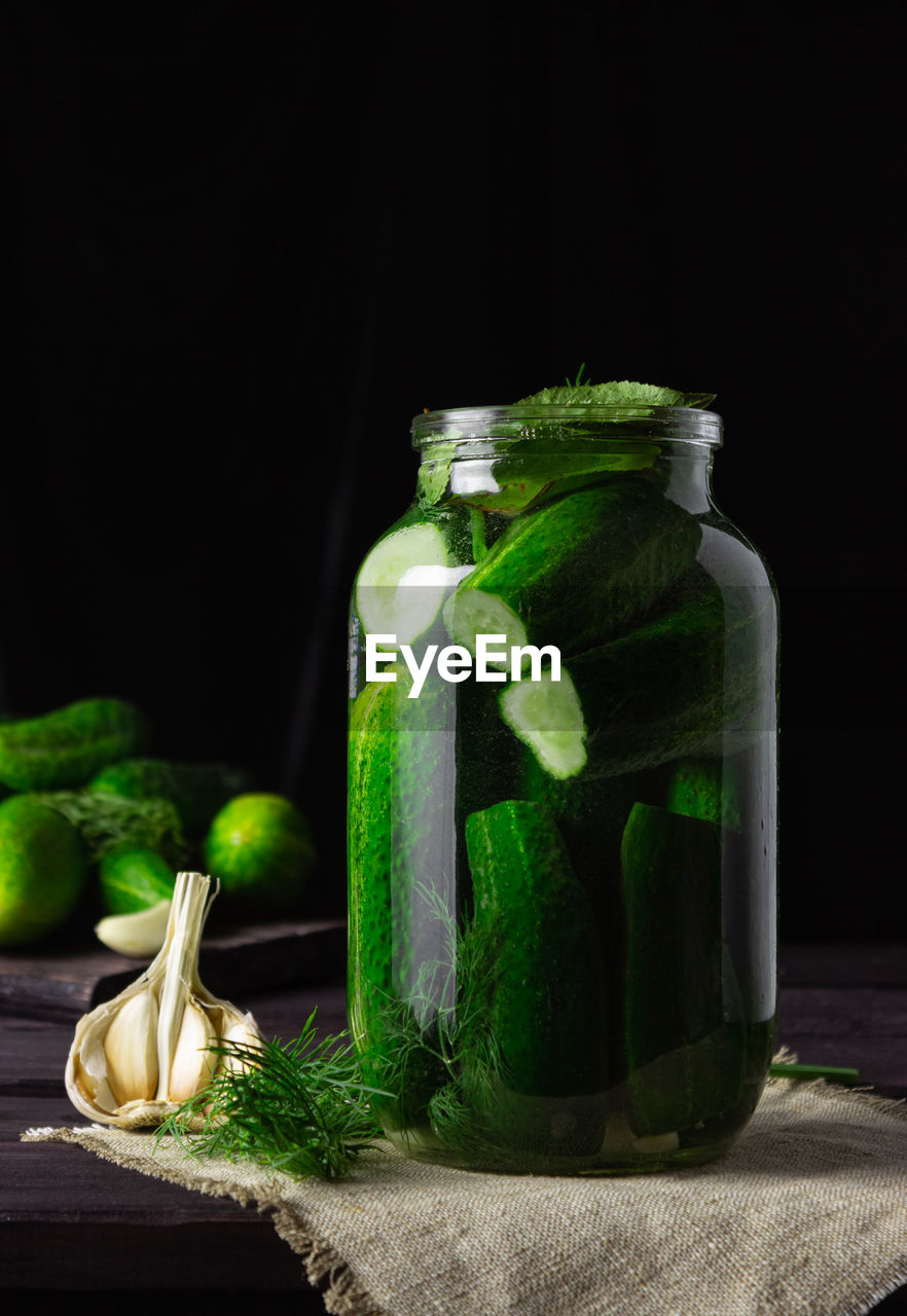 Lightly salted cucumbers in a glass jar with garlic on a dark wooden table.