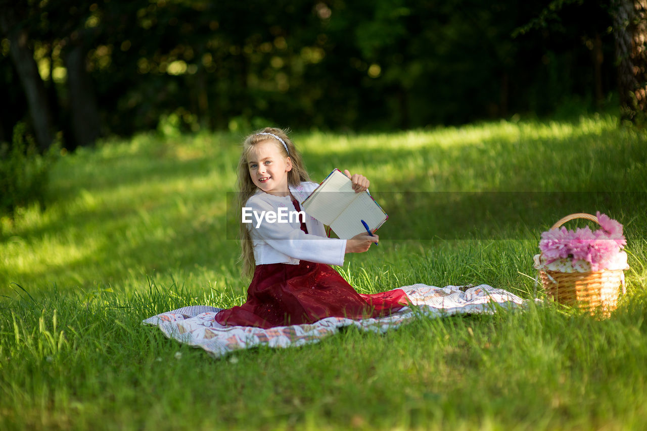 Portrait of girl holding book and pen while sitting on grass