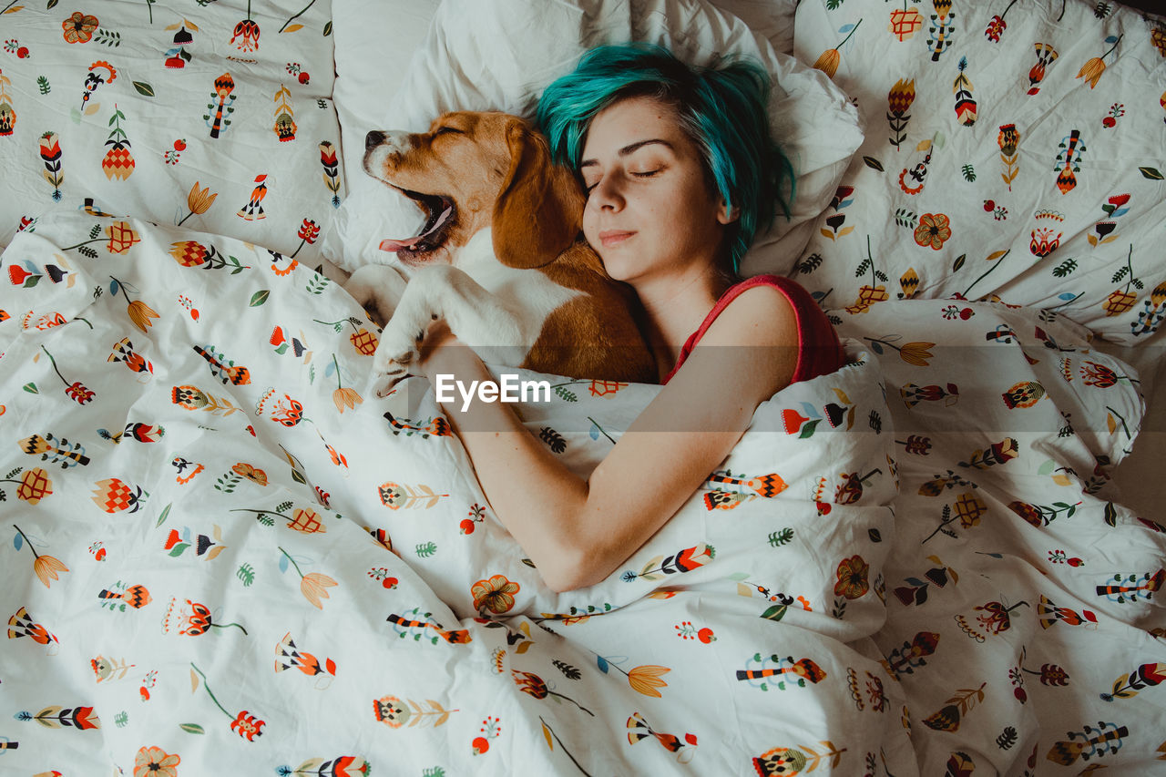High angle view of woman sleeping with dog on bed