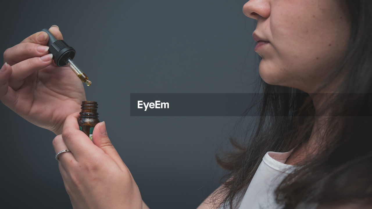 Side view midsection of woman taking medicine against gray background