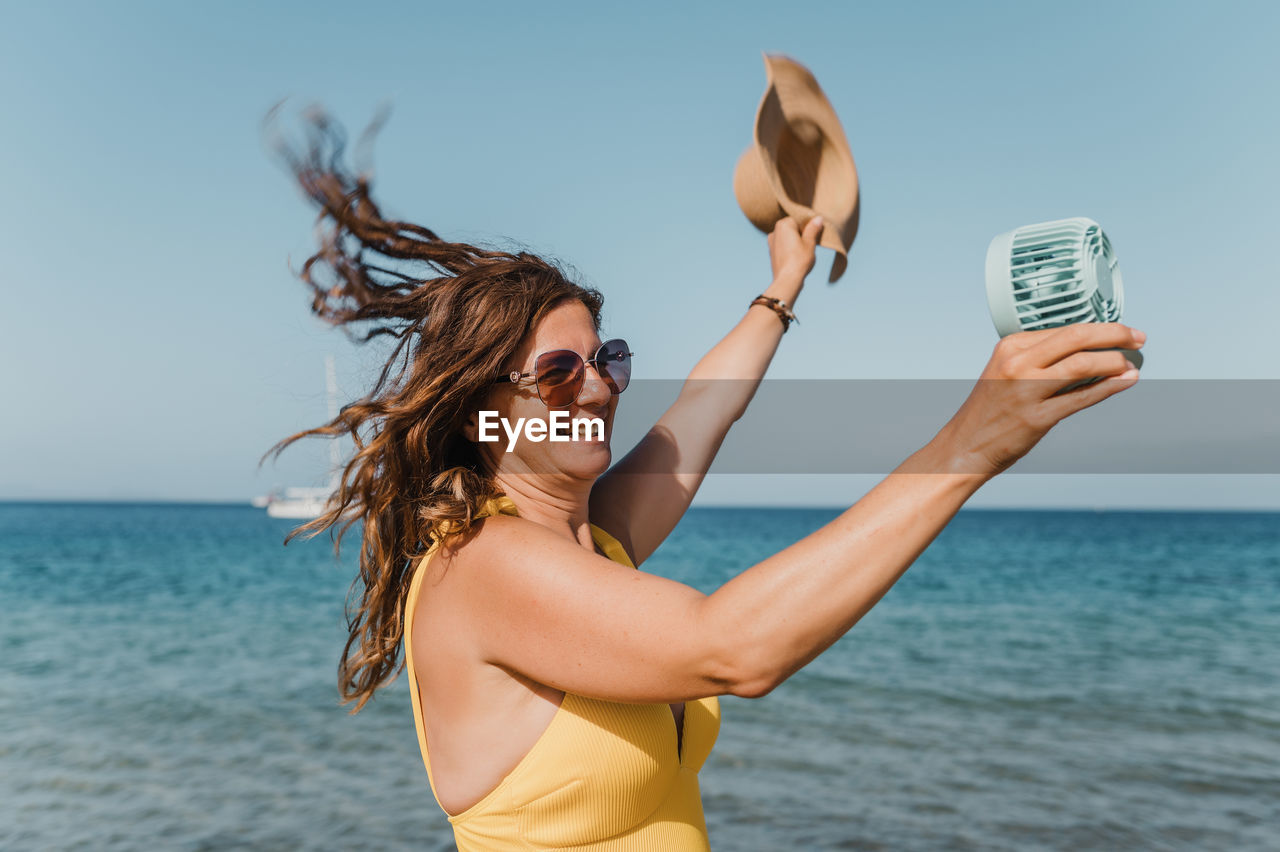 rear view of young woman holding water while standing at beach against sky