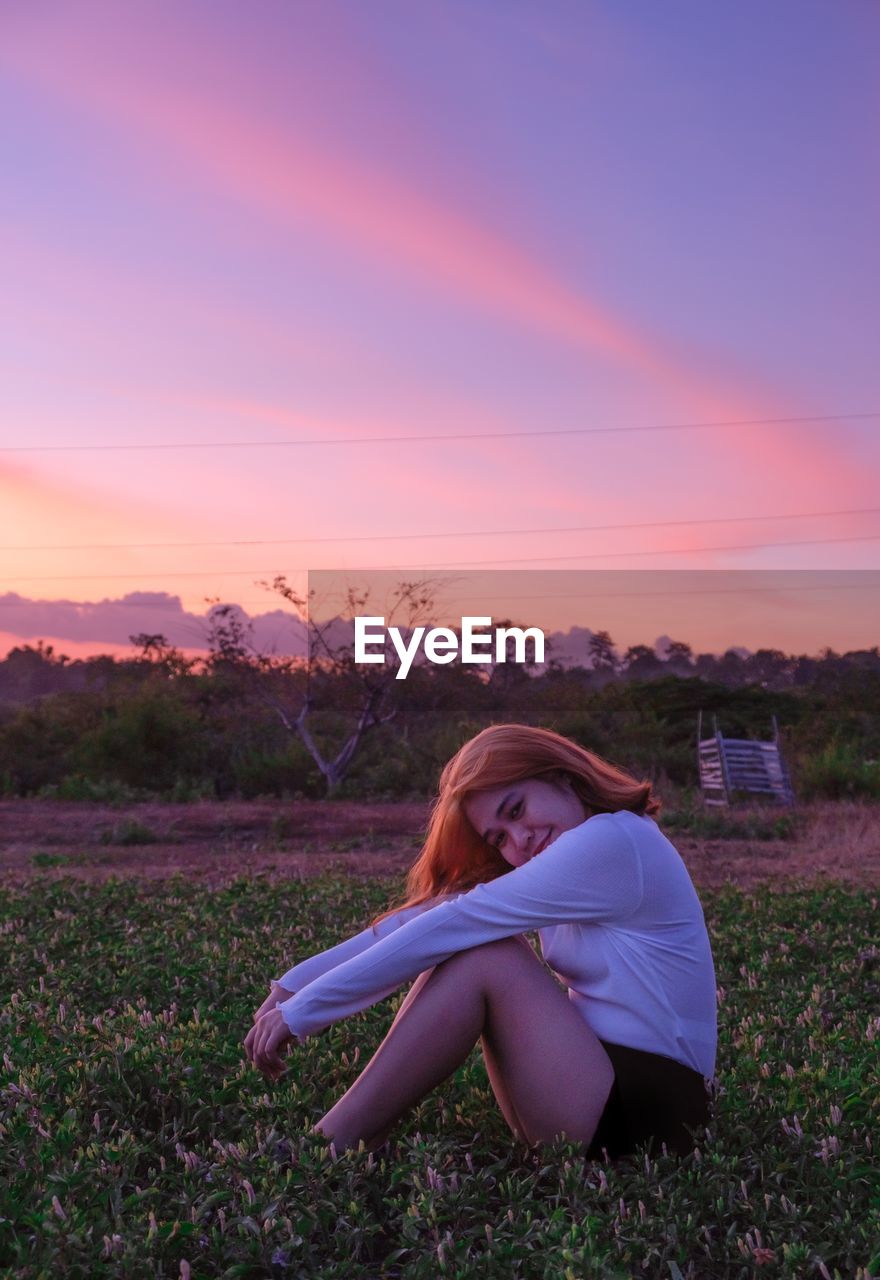 Woman sitting on field during sunset