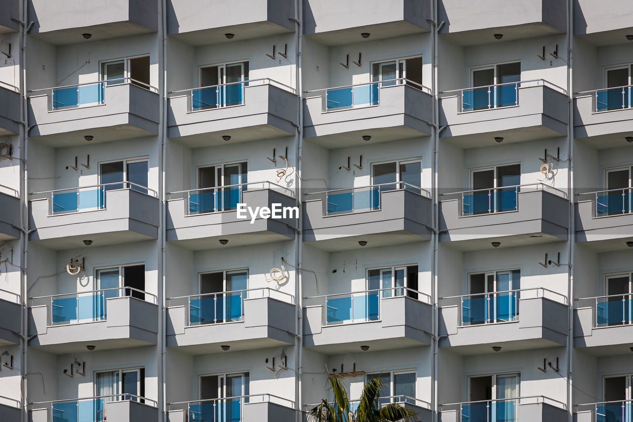 A white residential building with flat, identical balconies with ripped air conditioners