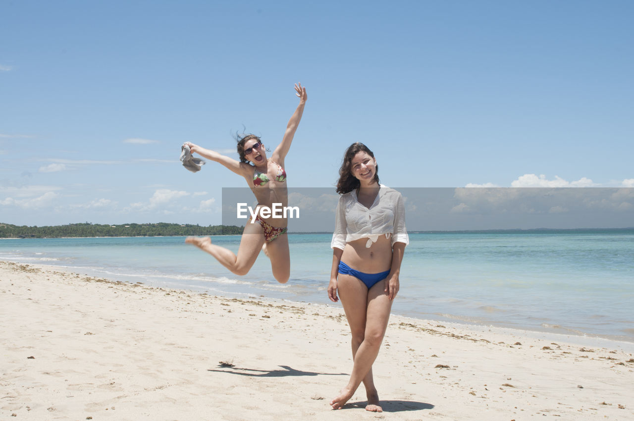 Portrait of happy friends enjoying at beach against sky