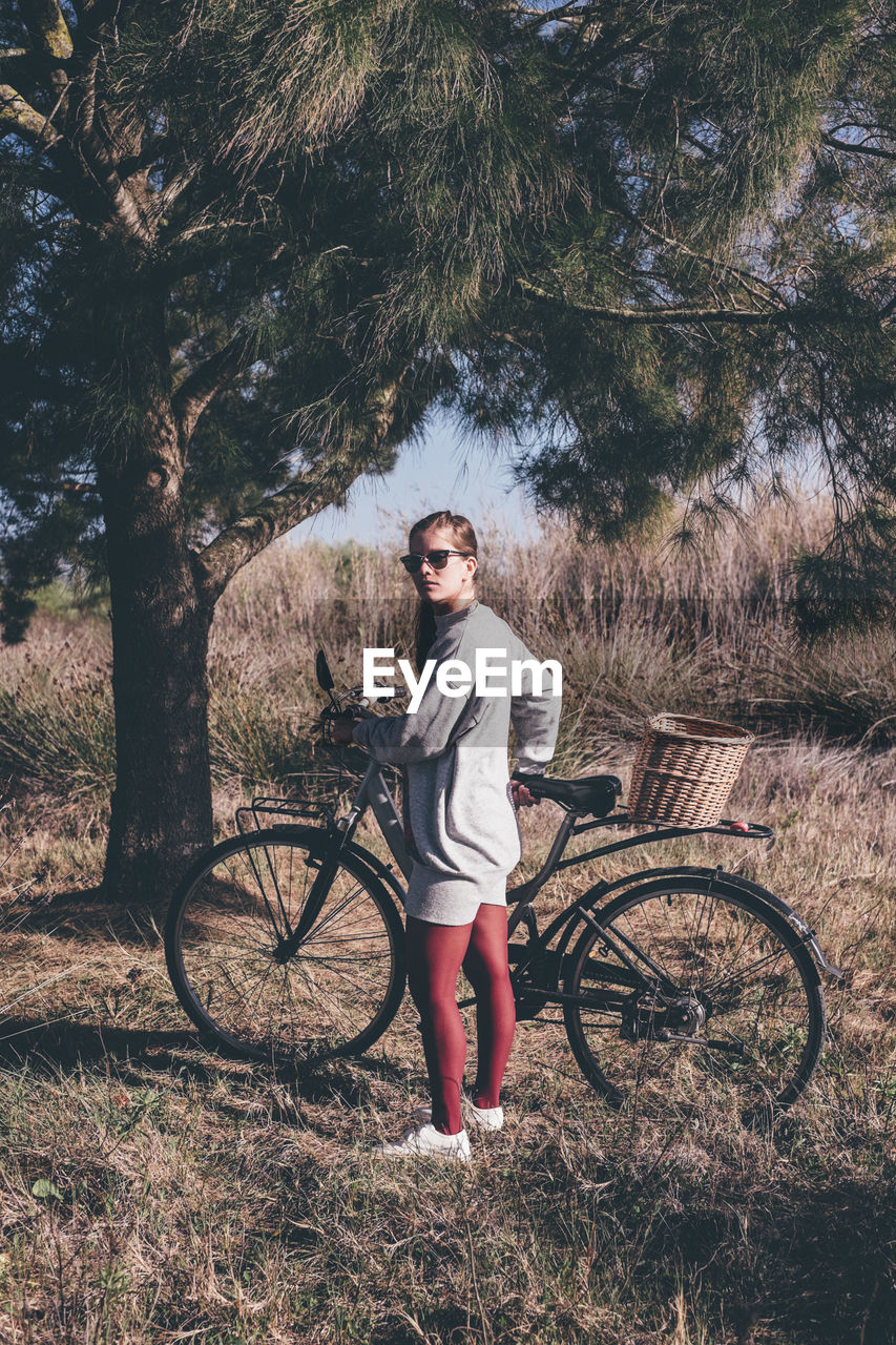 Portrait of young woman with bicycle standing on field