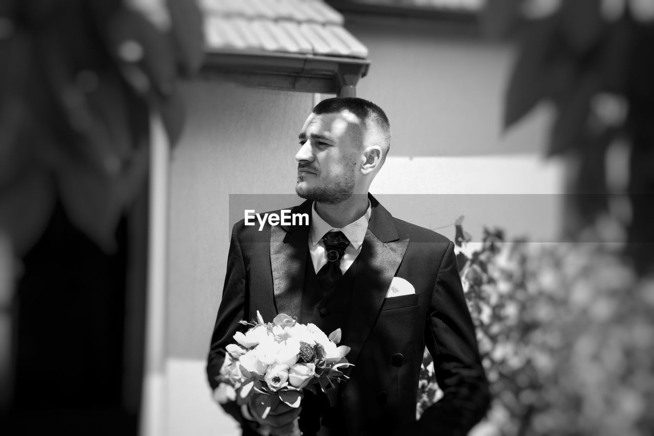 Groom holding bouquet while standing outdoors