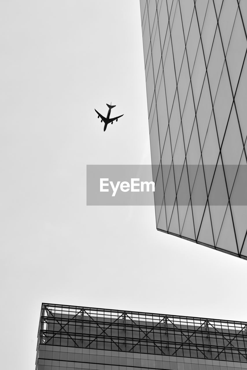 Low angle view of modern building against silhouette airplane flying in clear sky