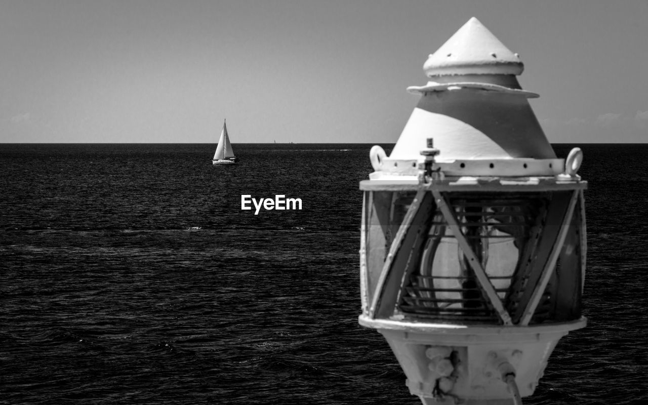 Sailboat sailing next to lighthouse on sea against sky