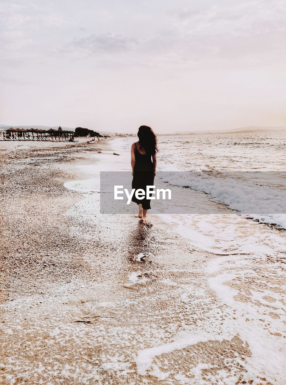 Rear view of woman standing on beach against sky