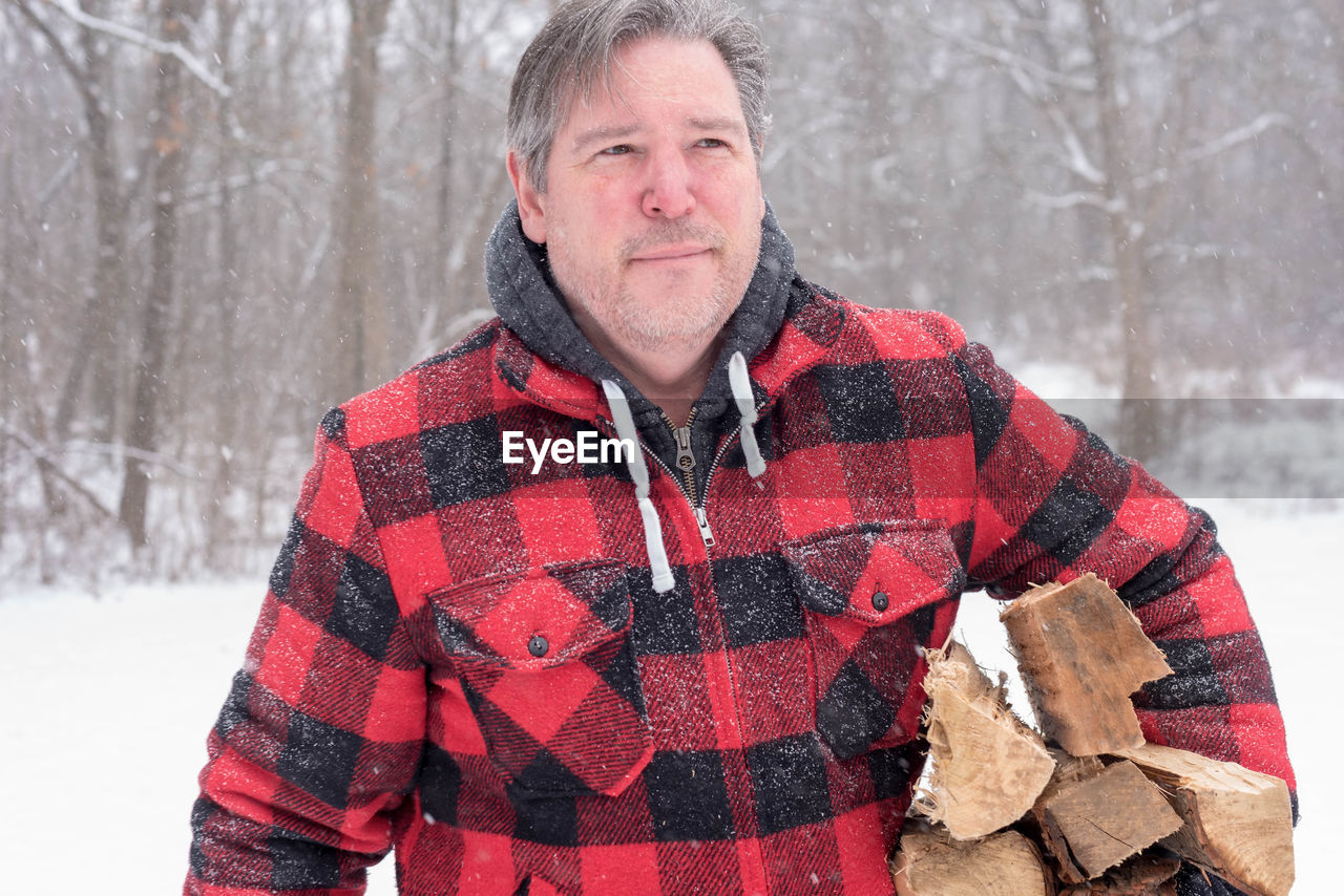 Midsection of mature man with wood during snowfall