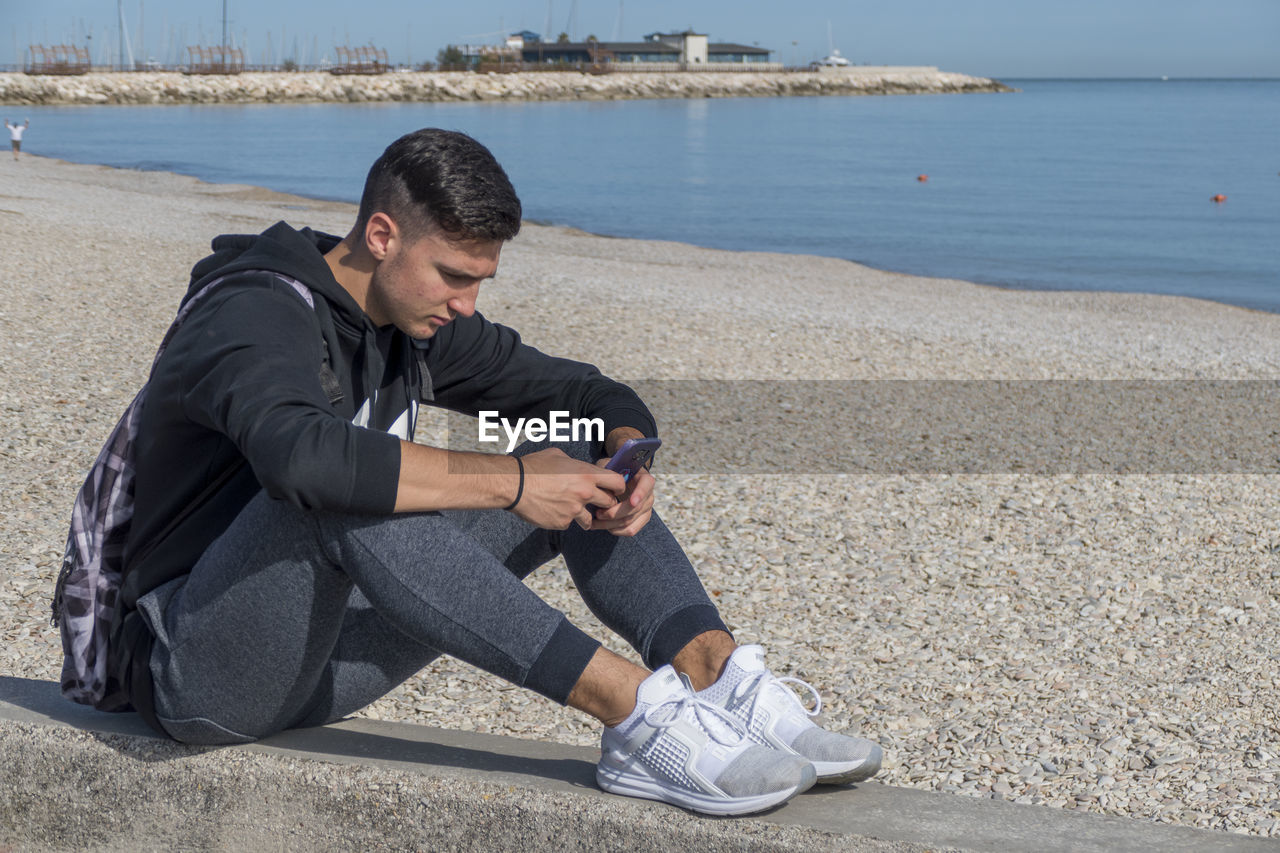 Young man using mobile phone while sitting on beach