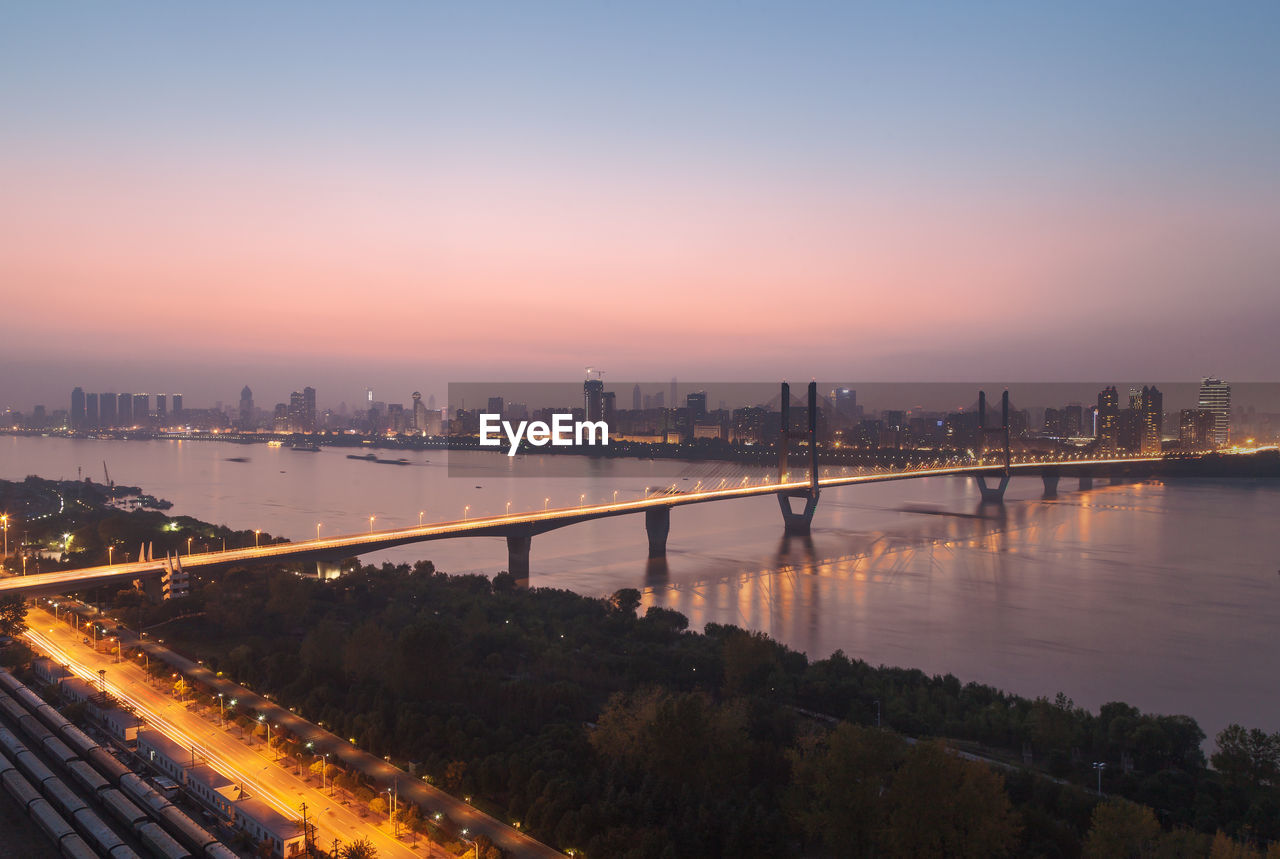 Illuminated bridge over river against sky at sunset