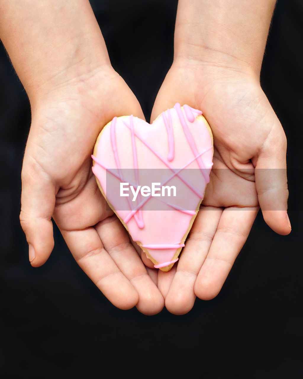 Cropped image of person holding heart shape cake against black background