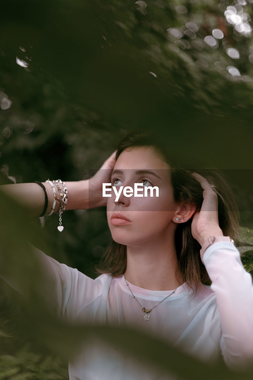 Young woman looking away while standing against trees