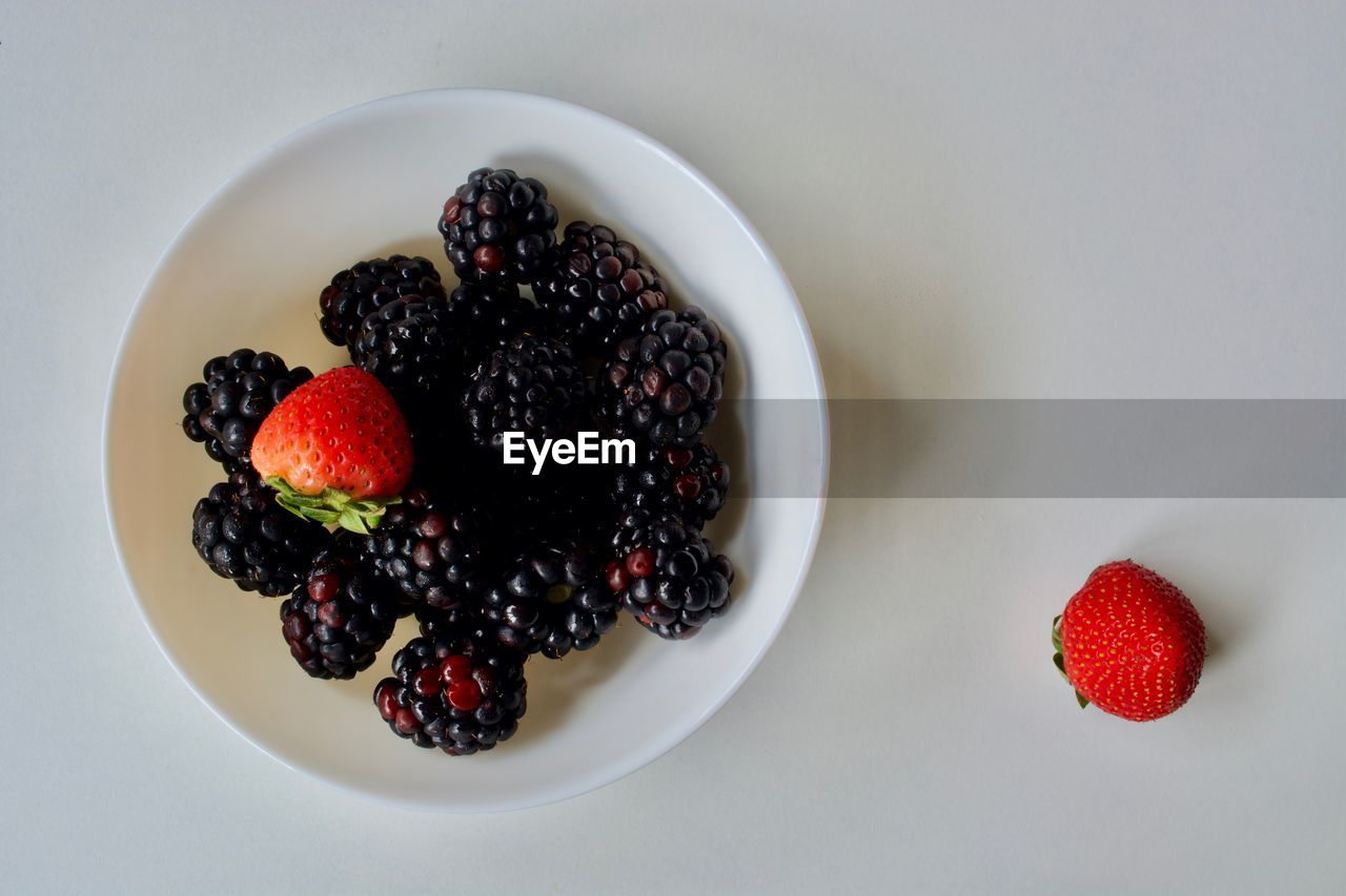 High angle view of strawberries with blackberries in bowl on white background