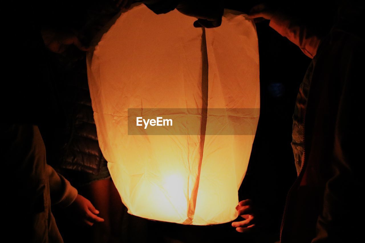 Midsection of male friends holding illuminated paper lantern at night