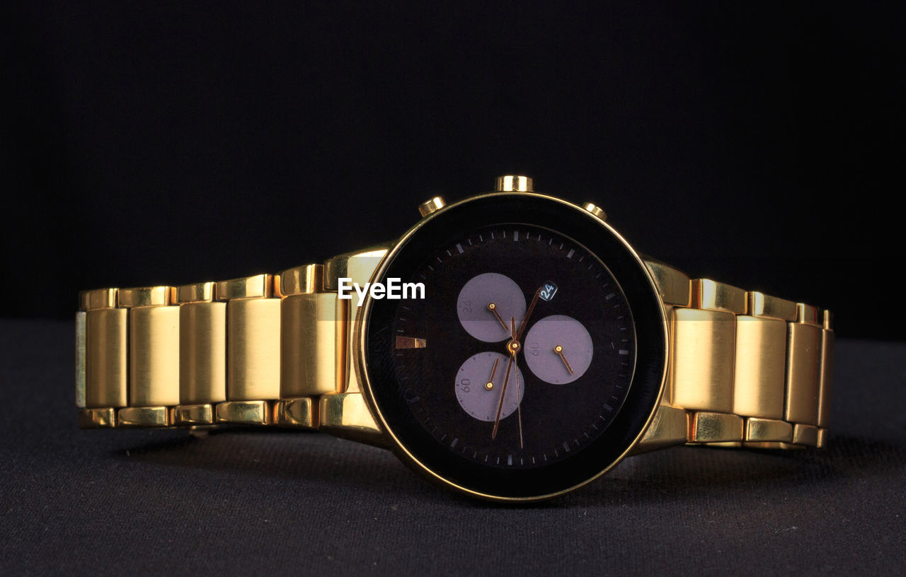 Close-up of watch on table against black background