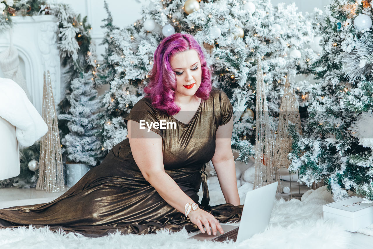 portrait of young woman sitting by christmas tree