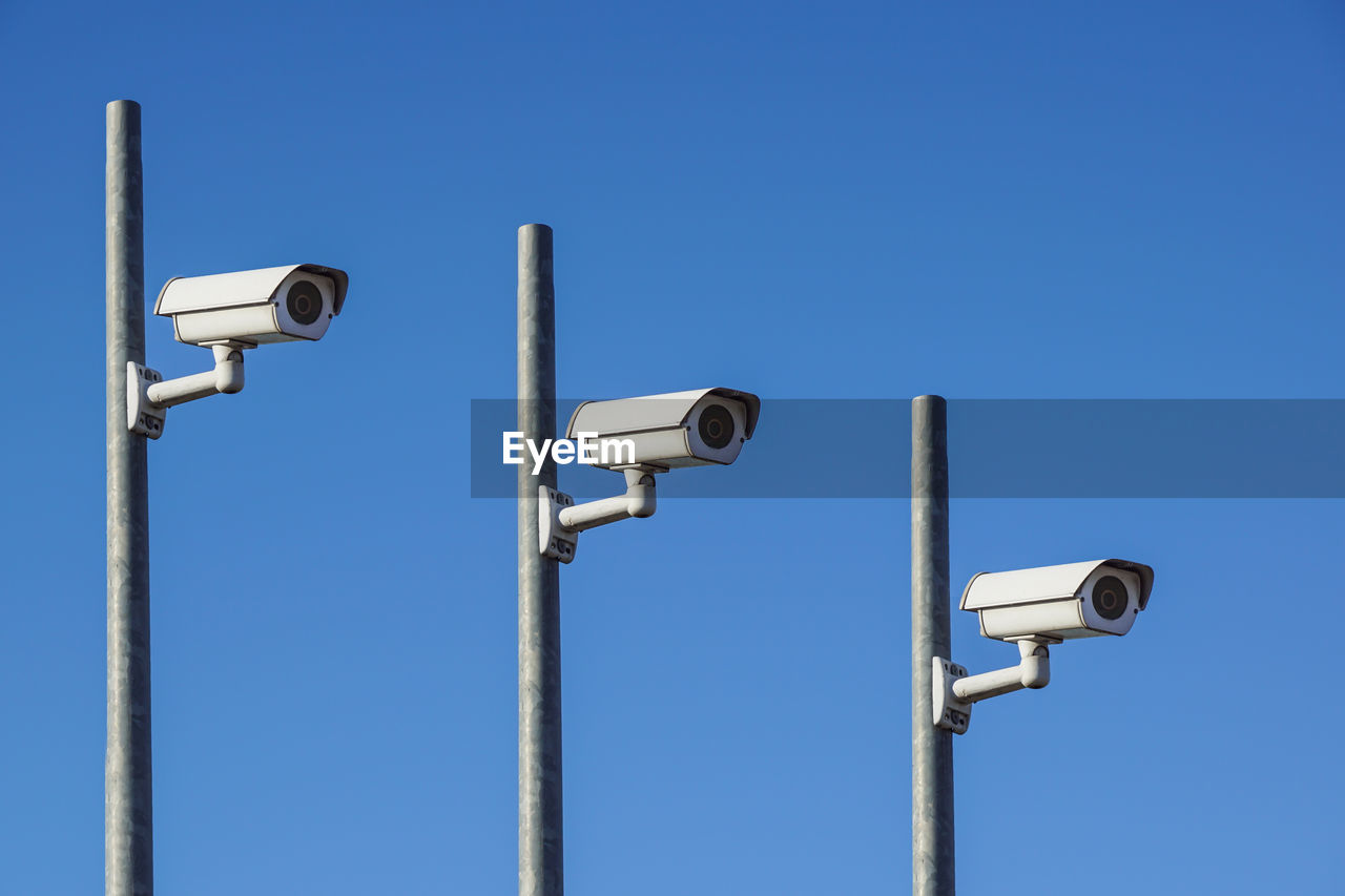 Low angle view of security cameras on pole against clear blue sky
