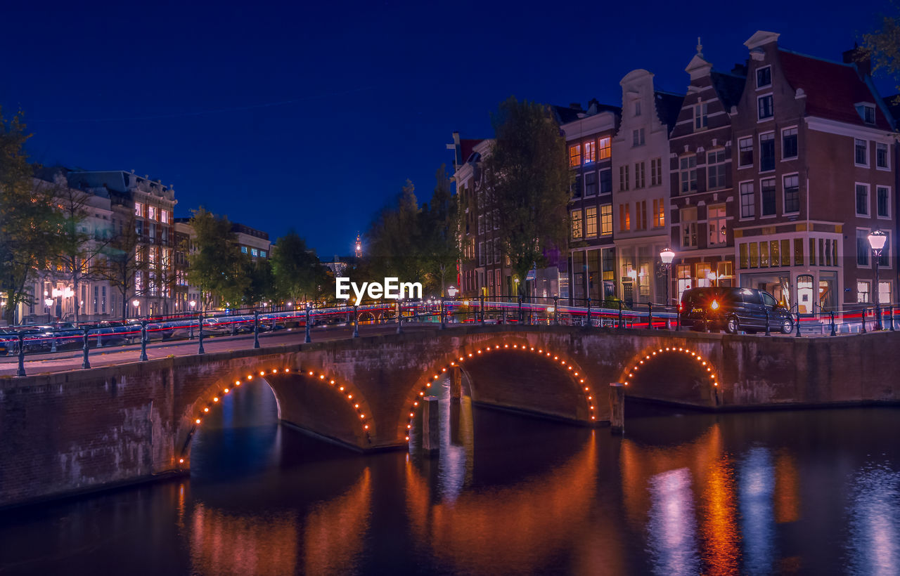 Bridge over canal amidst illuminated buildings in city at night