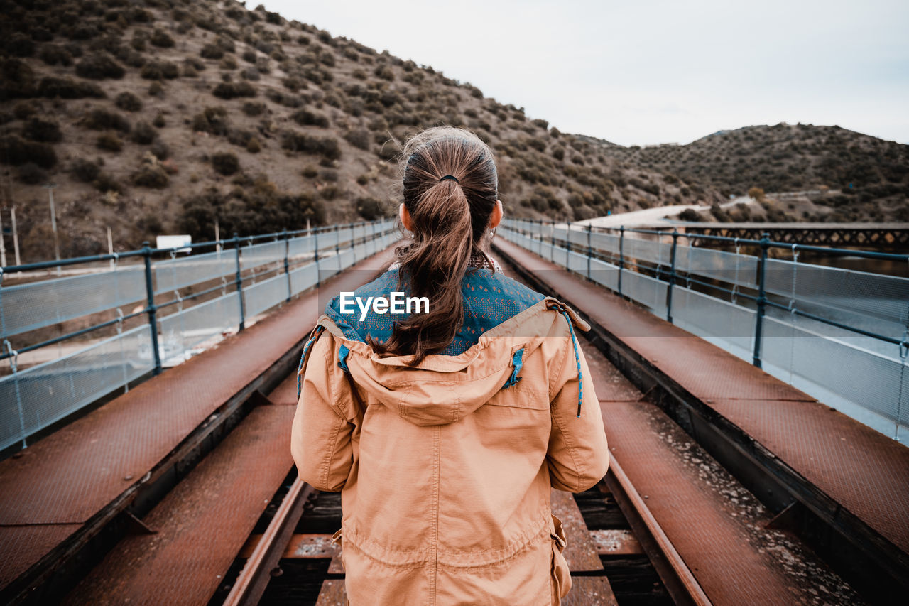 REAR VIEW OF WOMAN ON RAILROAD TRACK