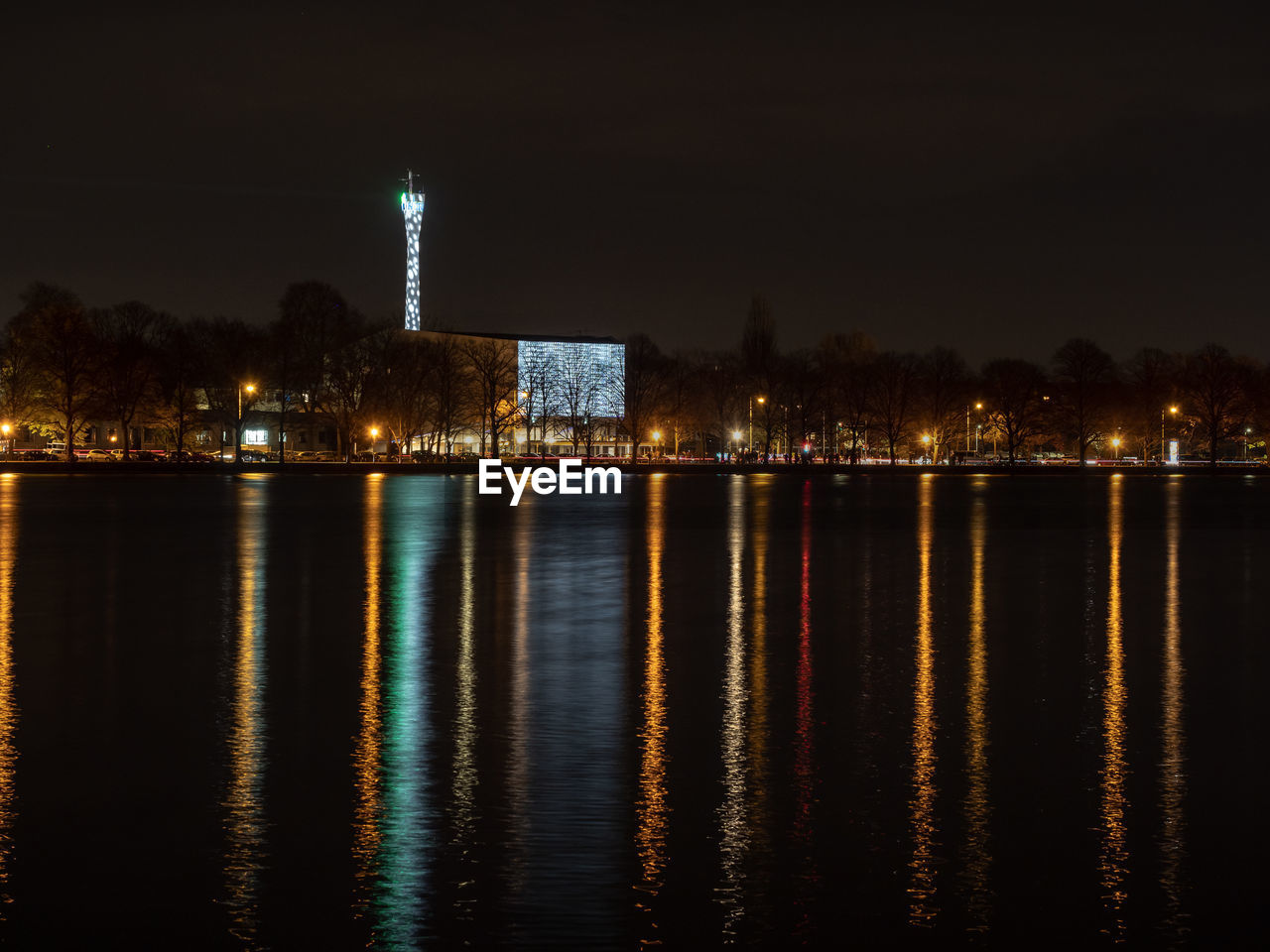 Illuminated buildings by river against sky at night