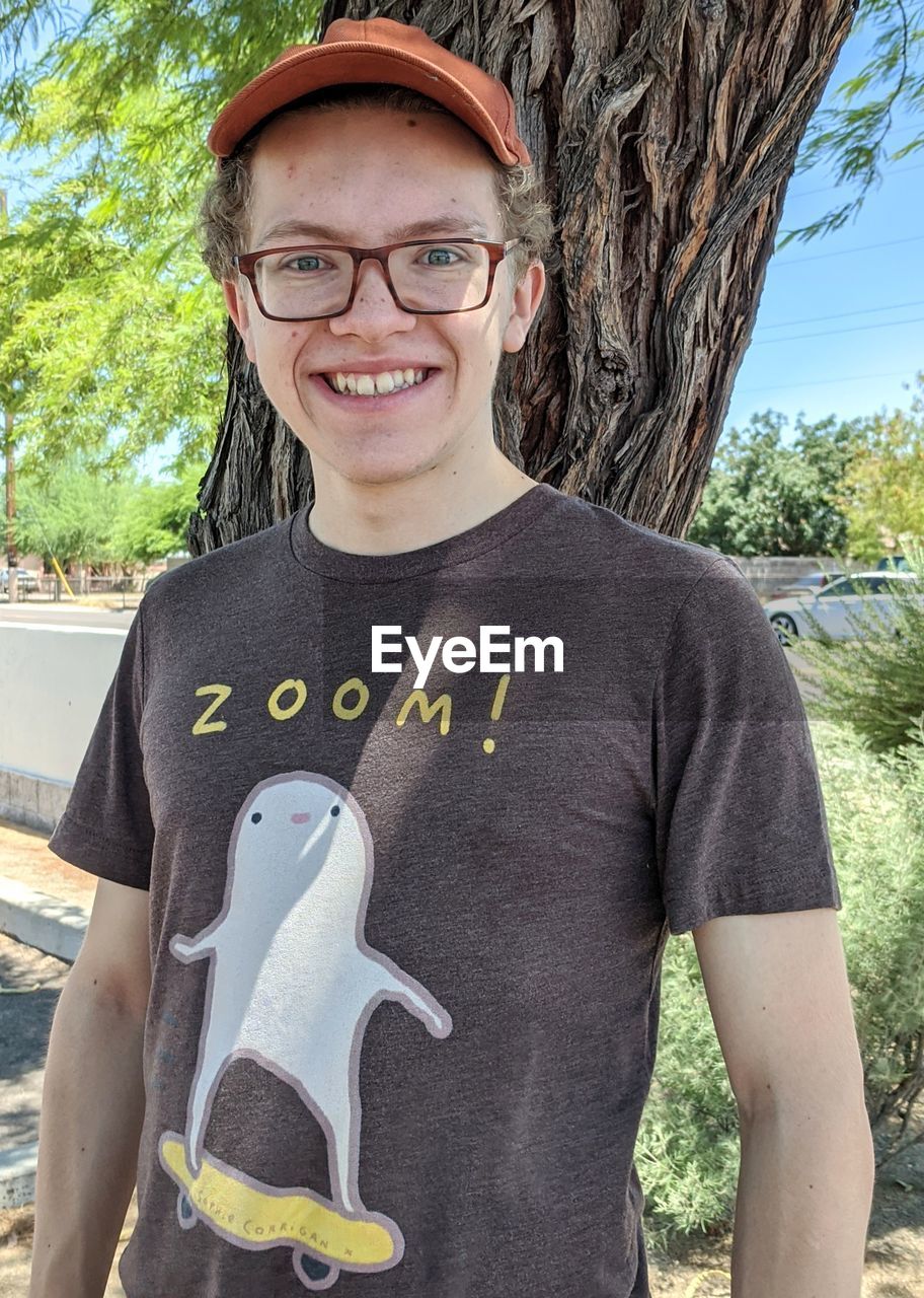 Portrait of smiling teenage boy posing in front of a tree