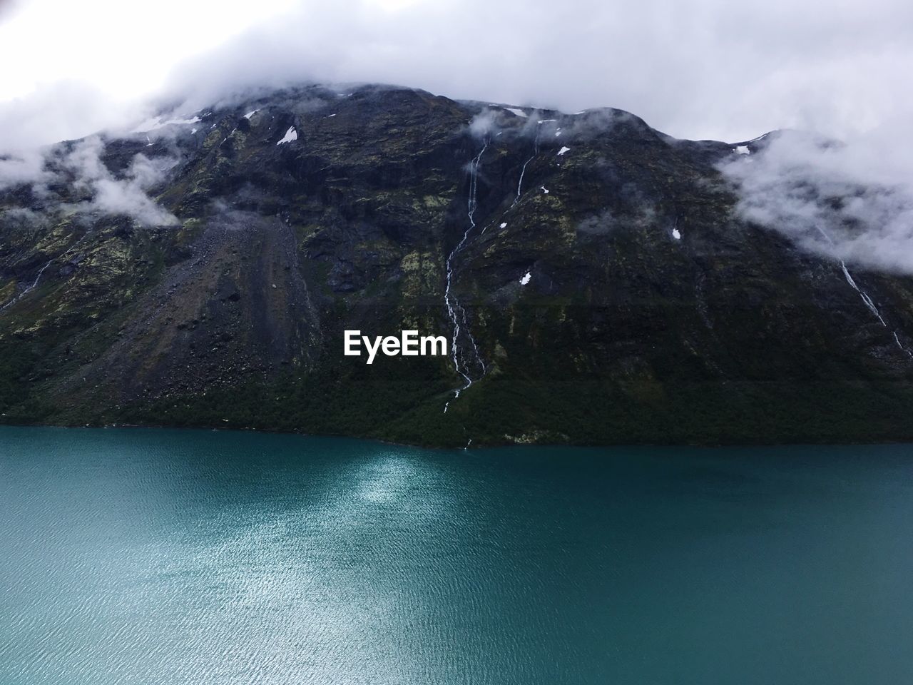 Scenic view of sea by mountain against sky