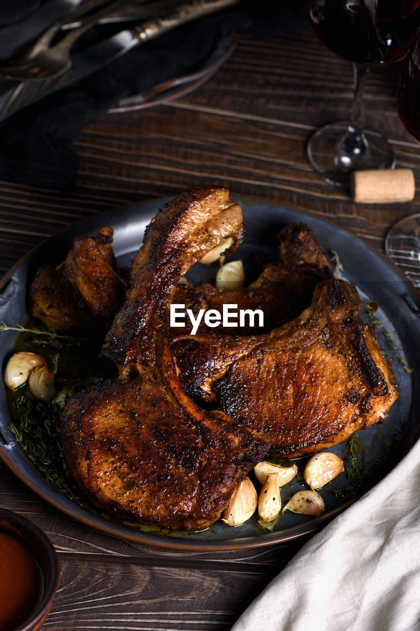 Juicy, slice of fried pork chop on a bone in oil with garlic and herbs in a pan. close-up.