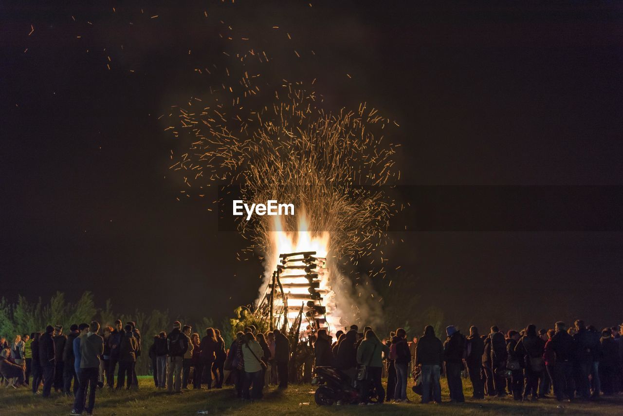People standing by bonfire against sky at night