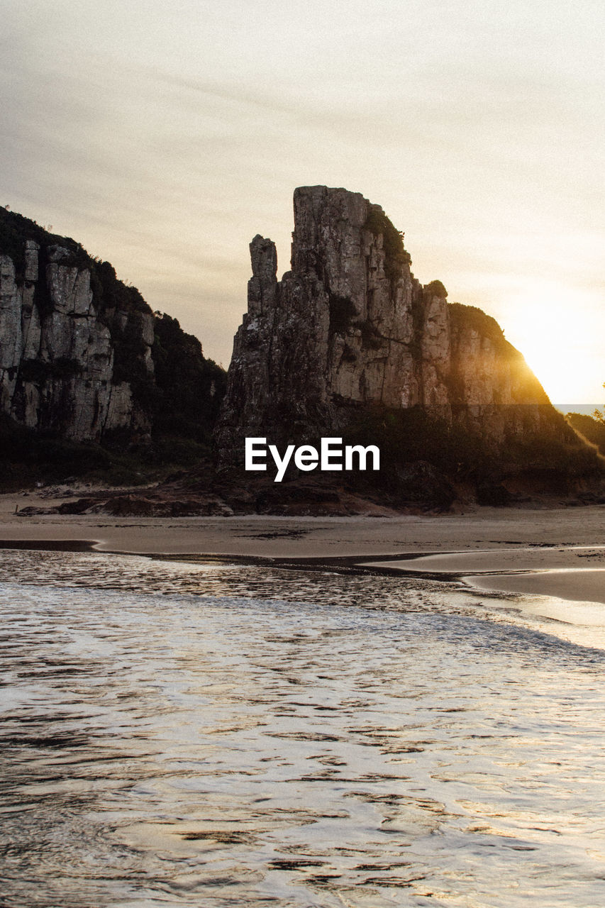 Rock formations on beach against sky during sunset