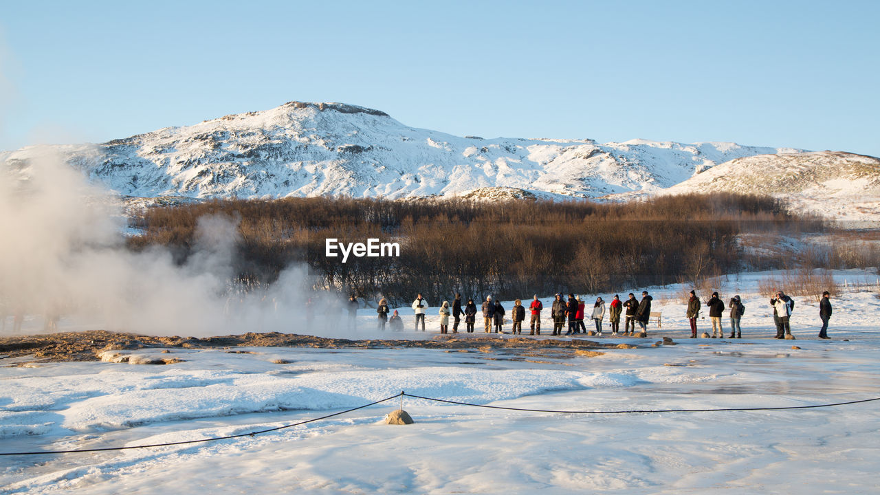 People standing by hot spring against snowcapped mountain