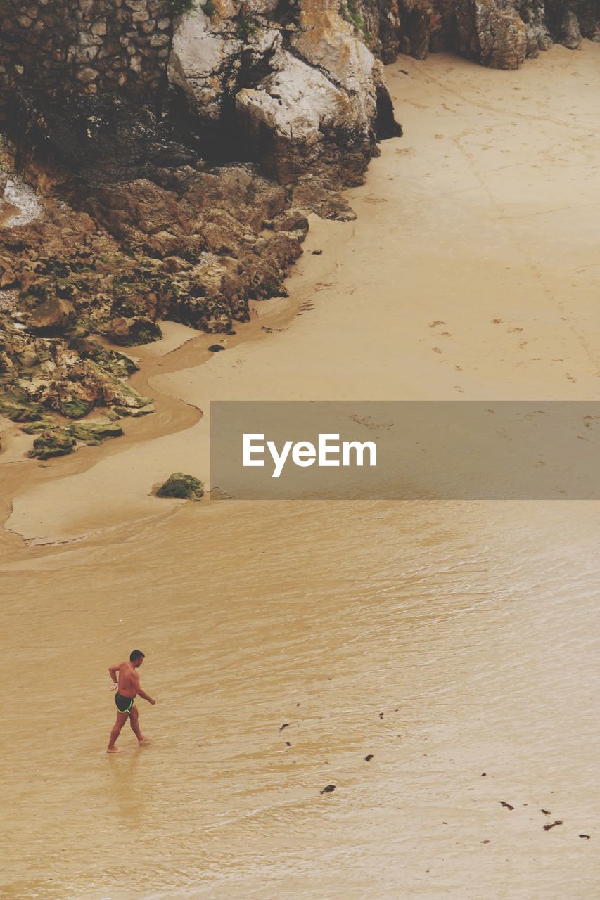 High angle view of shirtless man walking at sandy beach