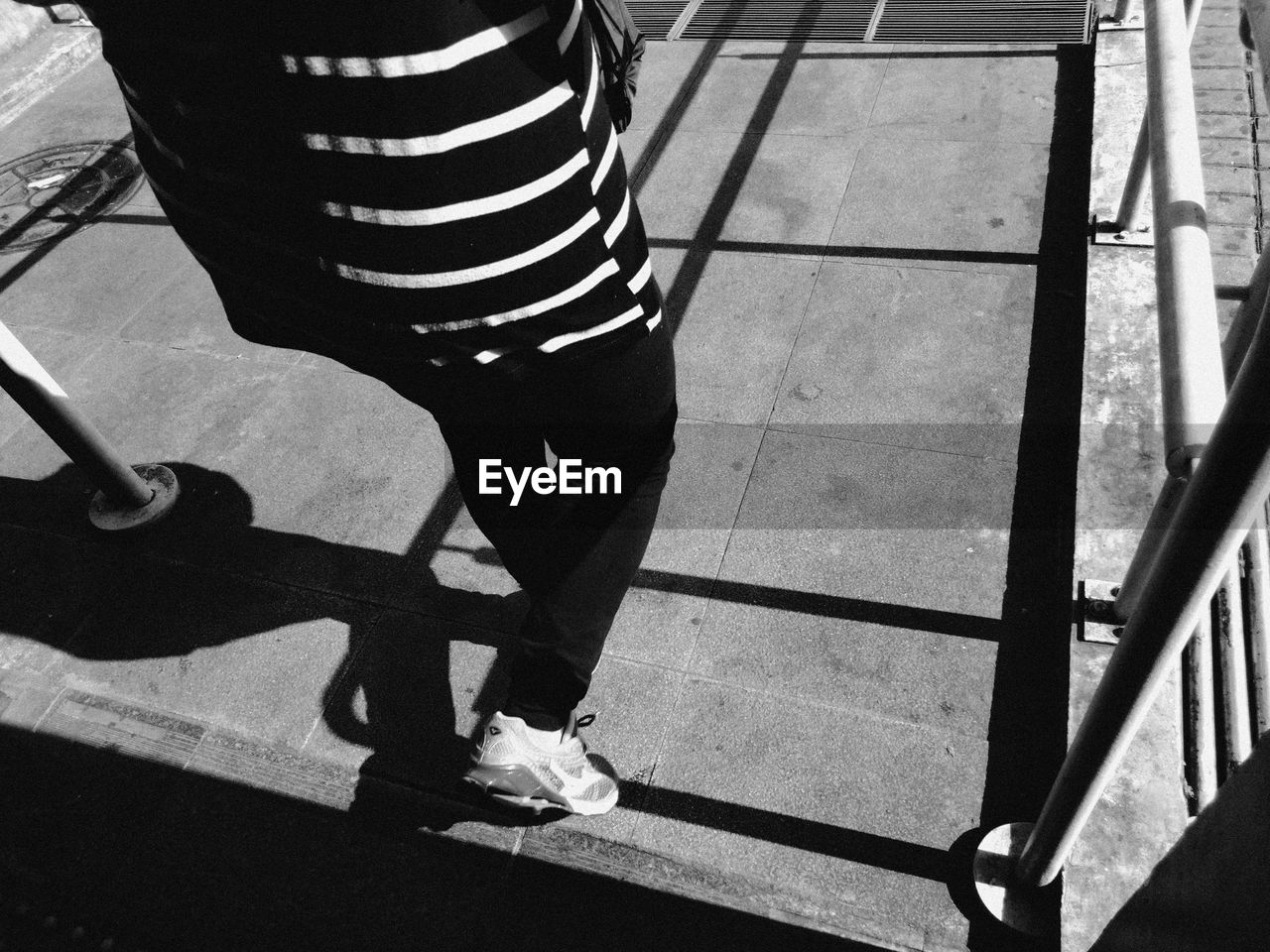 LOW SECTION OF WOMAN STANDING ON TILED FLOOR WITH SHADOW