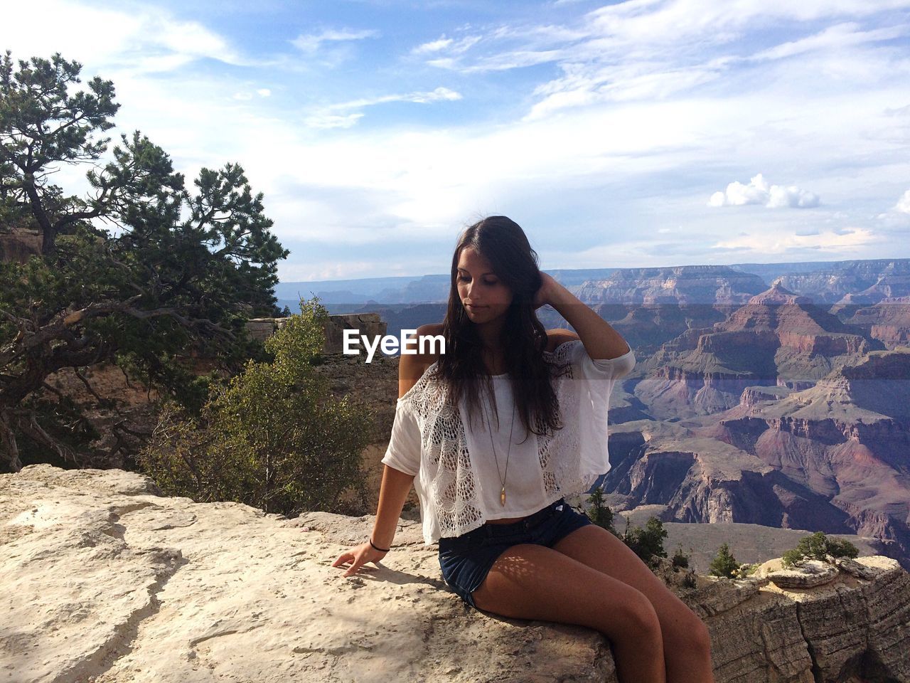 Woman relaxing on rock formation against cloudy sky at grand canyon