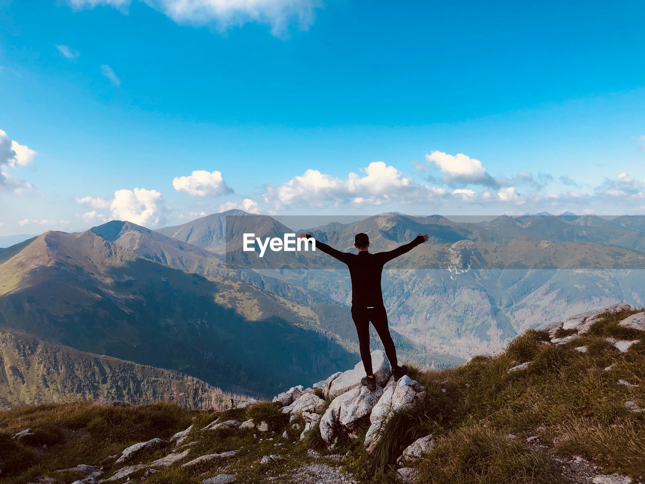 Rear view of man with arms outstretched standing on mountain against sky