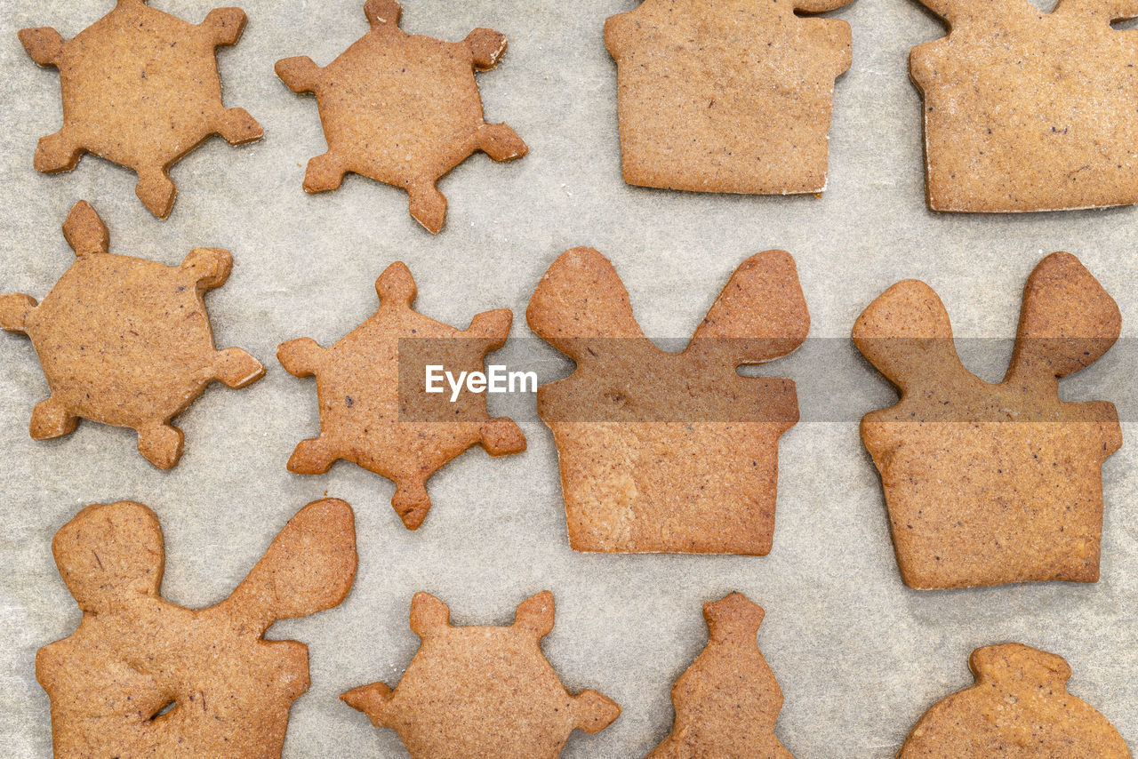 Baked gingerbread cookies in various shapes without decorations, lying on baking paper, top view.