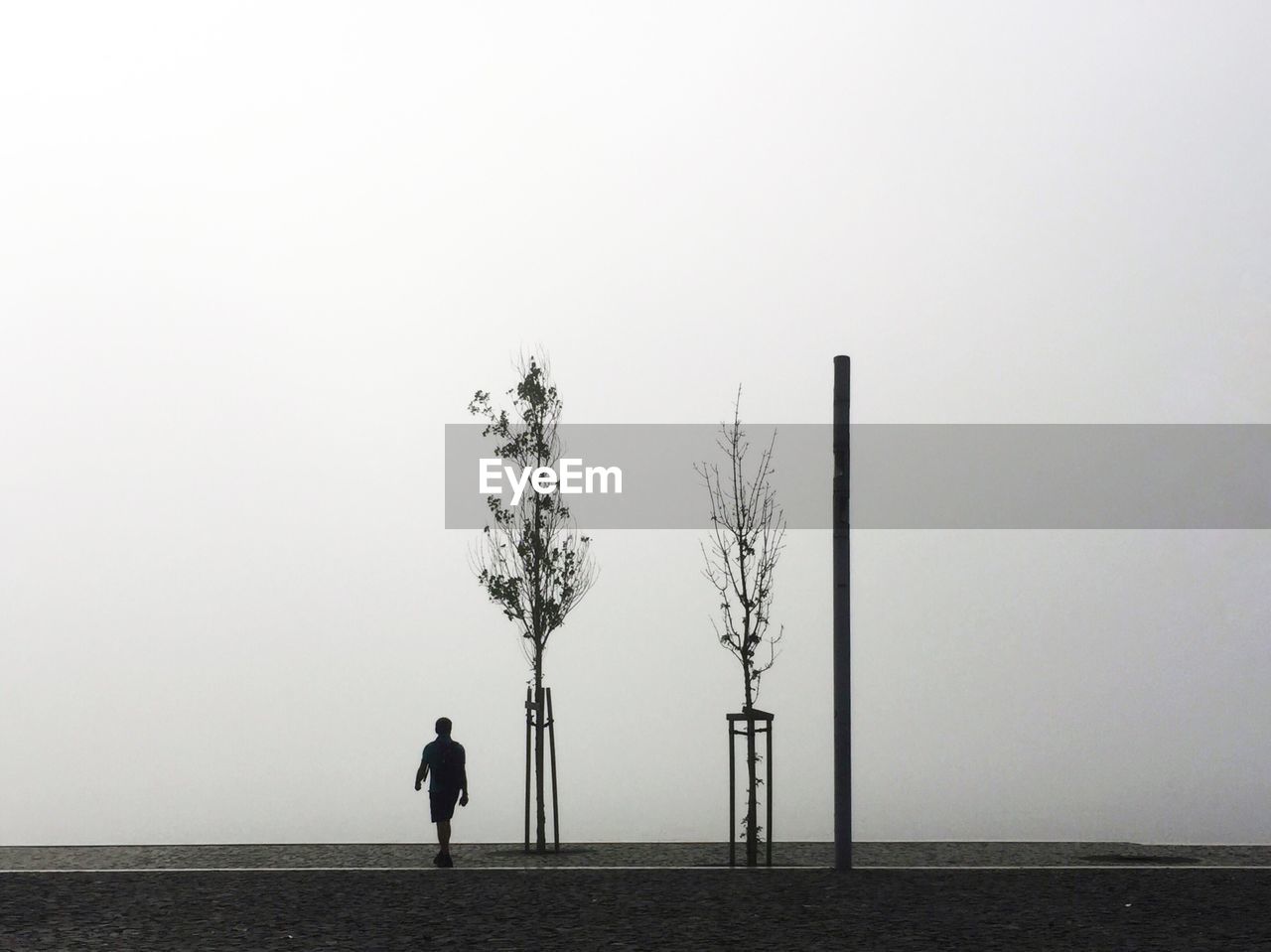 Silhouette man walking on footpath against sky during foggy weather