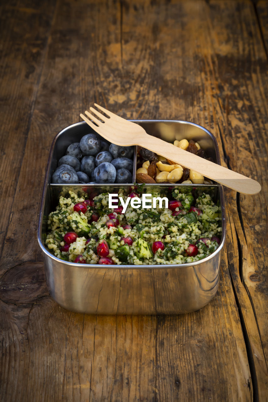 Lunchbox with bulgur herbs salad with pomegranate seeds, taboule, blueberries and trail mix