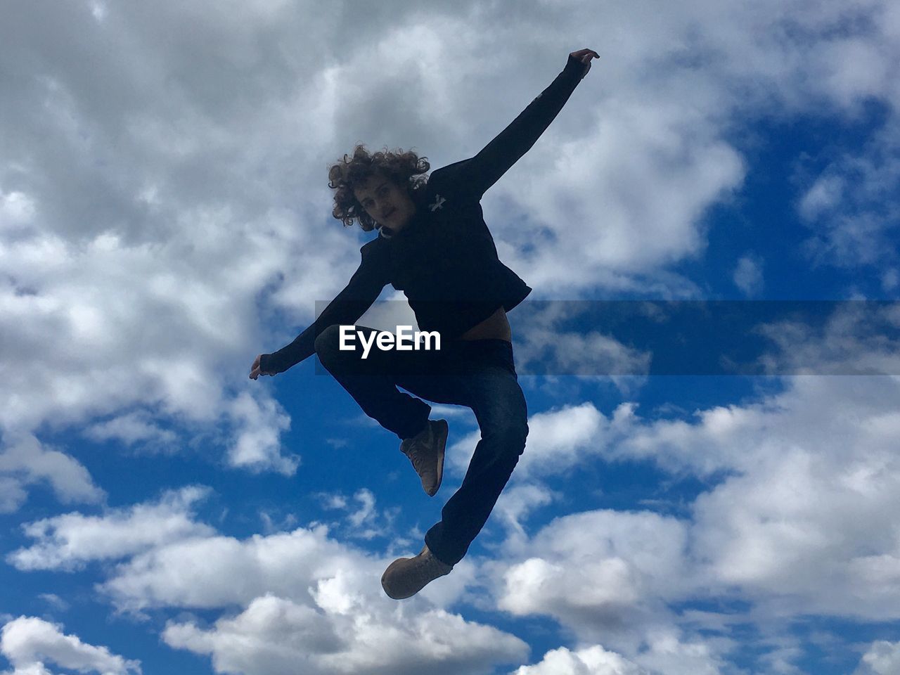 LOW ANGLE VIEW OF YOUNG WOMAN JUMPING AGAINST CLOUDY SKY