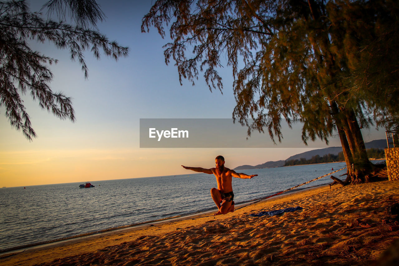 REAR VIEW OF WOMAN ON BEACH AT SUNSET