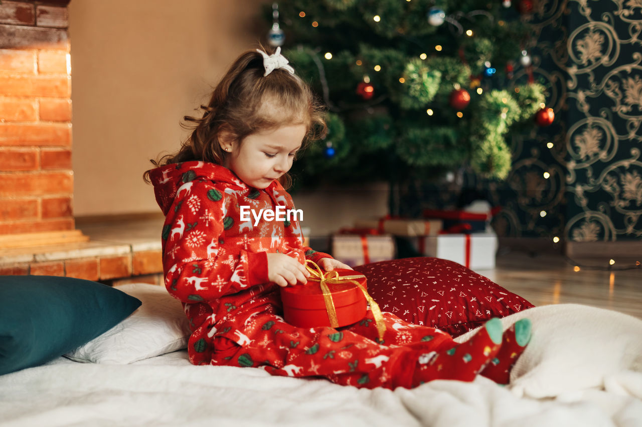 Little girl opens a christmas present near the christmas tree